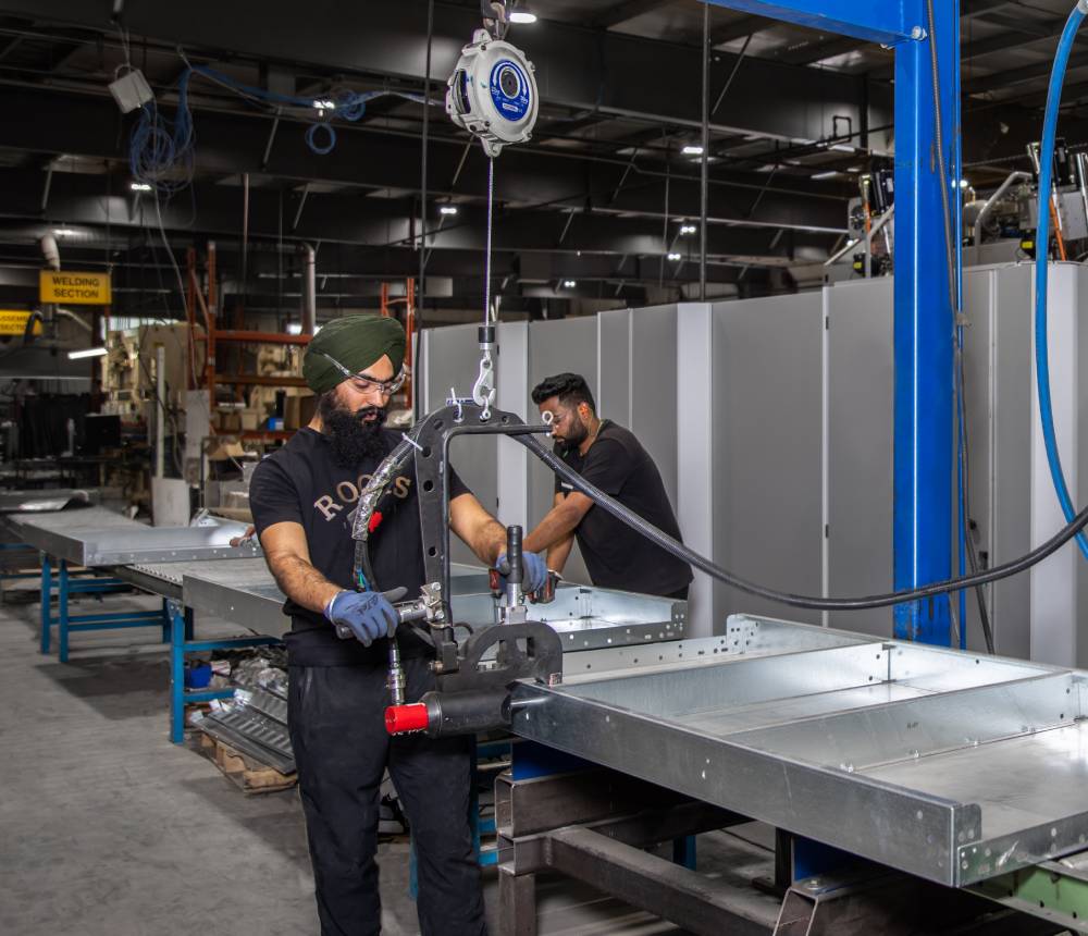 Two men wearing blue overalls operate a machine, focused on their task in an industrial environment.